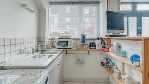 Una cocina compacta con microondas, cafetera y un televisor de pantalla plana sobre una estantería.