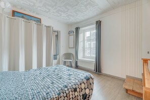 Ein Schlafzimmer mit einem Bett, einem Sessel, einer hölzernen Bank, einem Fenster mit Vorhängen, einer Heizung und einem Deckenventilator.