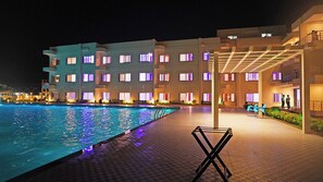 Ett hotell med en swimmingpool, flera balkonger och ett takförsett utomhusområde med stolar.