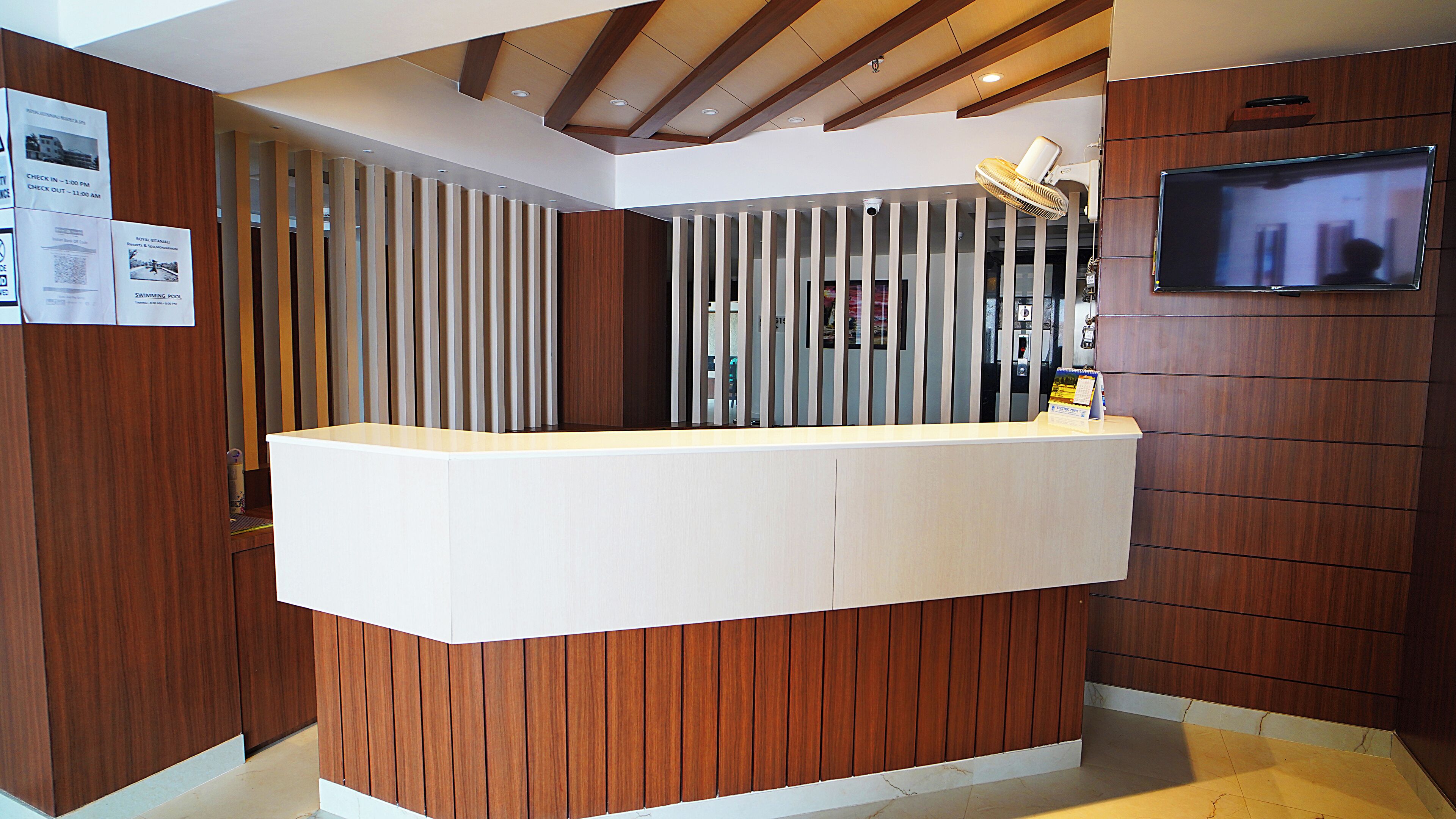 A reception desk with a wooden finish, a mounted television, and vertical blinds.