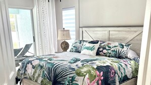 Une chambre à coucher avec un lit, un ventilateur de plafond, une fenêtre avec des rideaux et une vue sur l’extérieur.