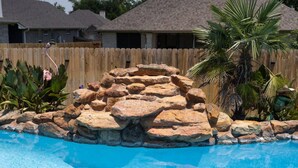 Una piscina con una isla rocosa rodeada de plantas tropicales.