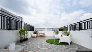 A rooftop patio with white furniture, potted plants, and a patterned floor. - Cove Taman (Jakarta)