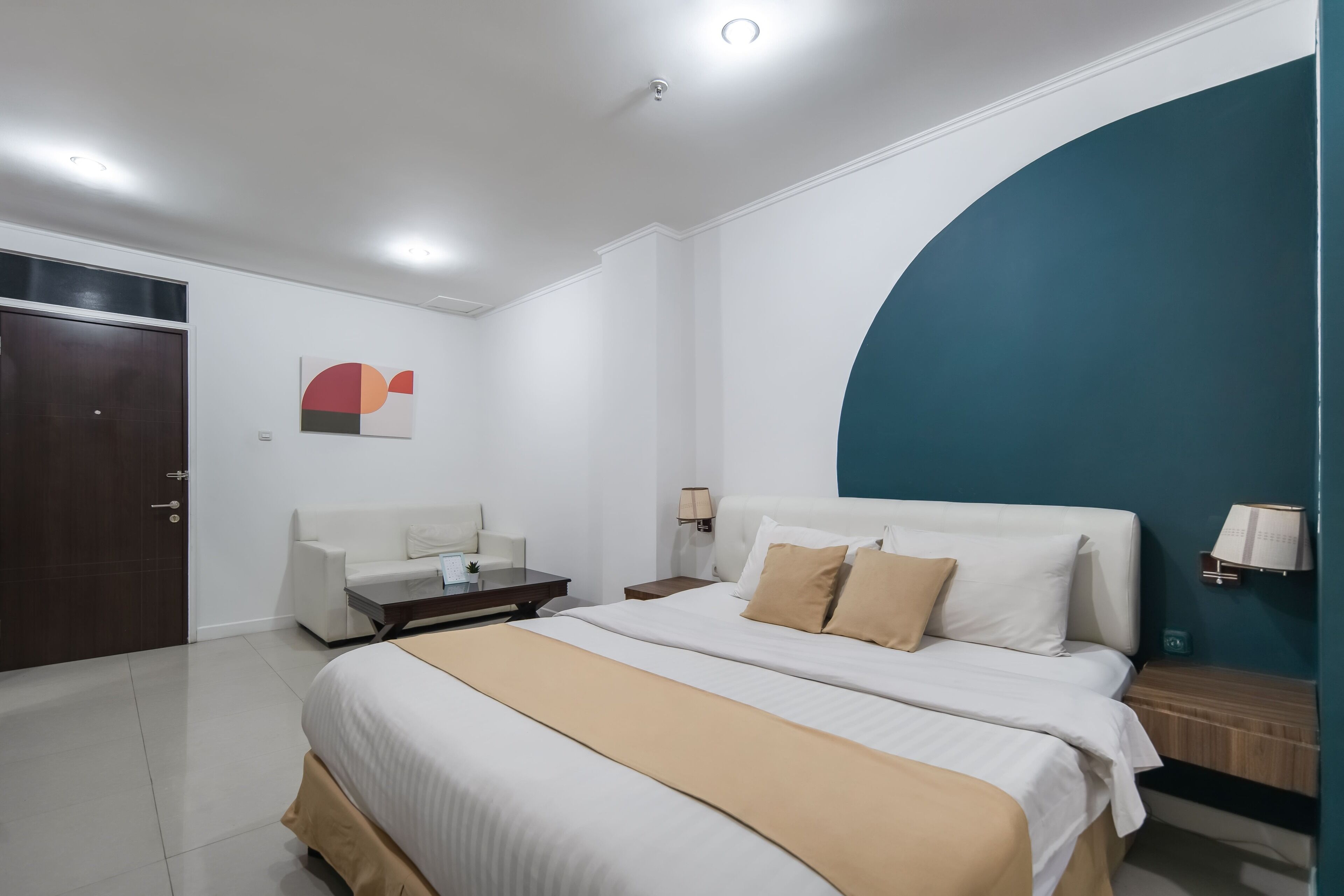 A hotel room with a large bed, a desk, a chair, and a wardrobe.