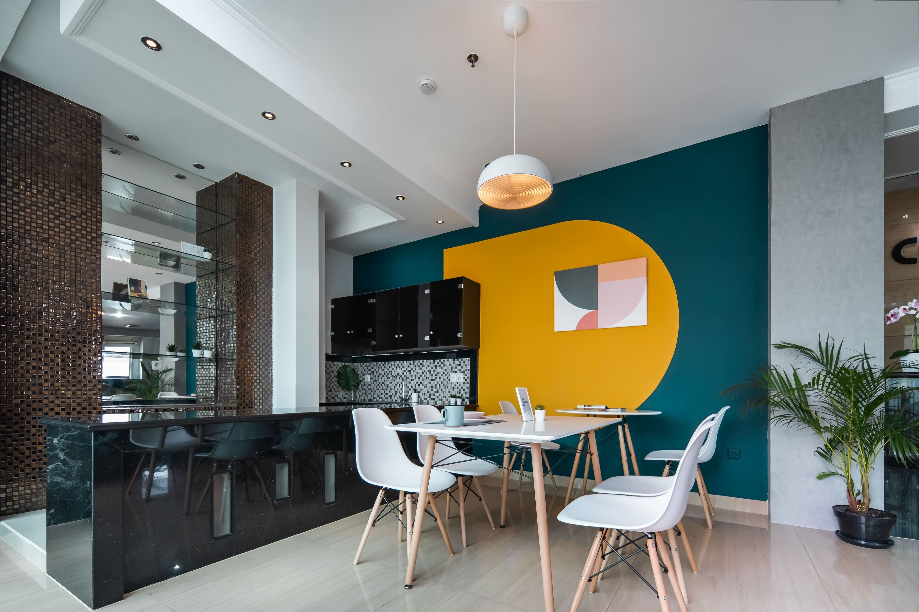 A modern kitchen with black cabinets, a central island, and a dining area with white chairs and a table.