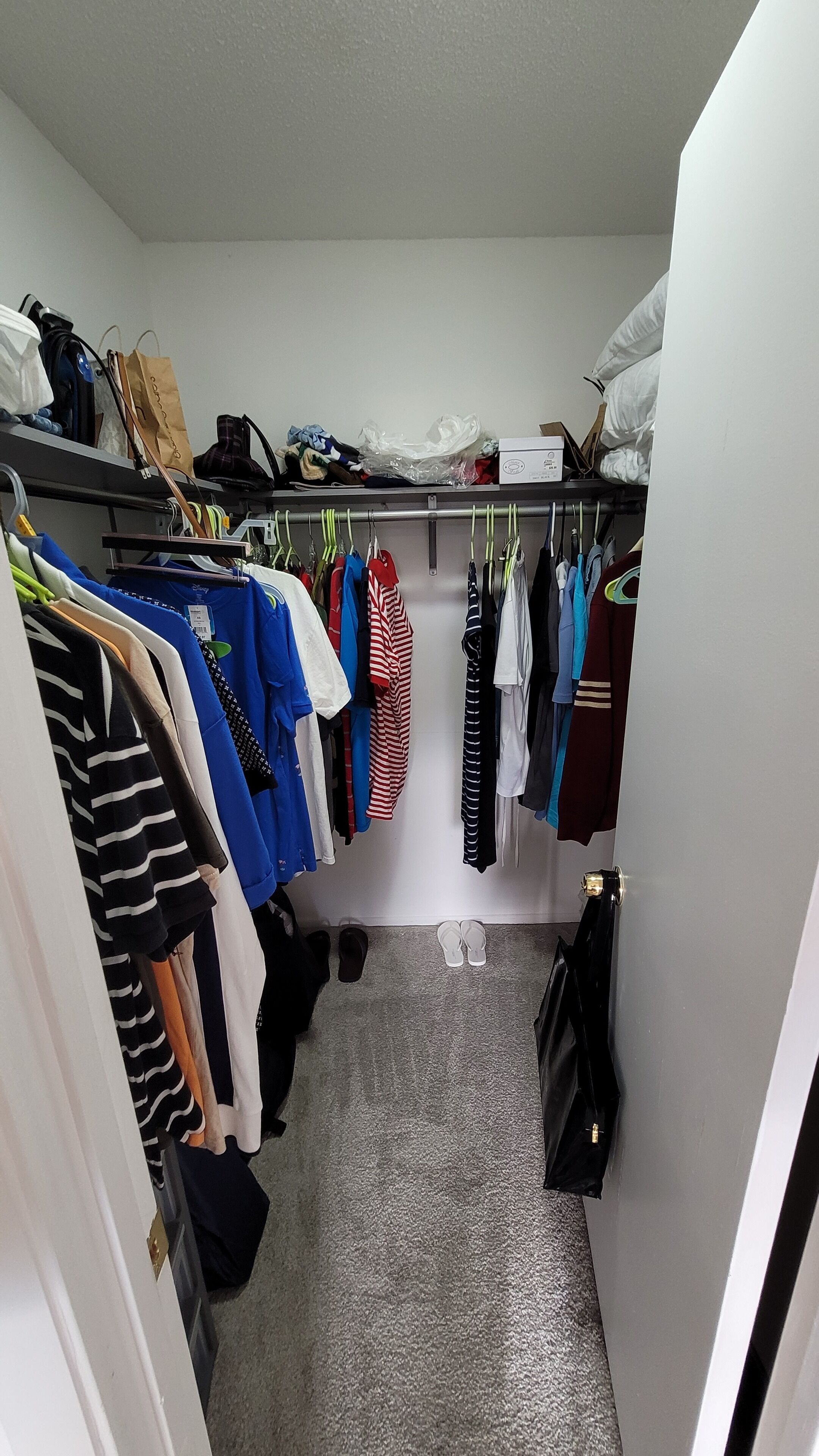 A narrow hallway with a closet containing hanging clothes and a few items on the floor.