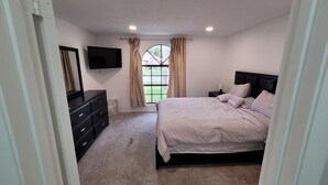 A bedroom with a bed, a dresser, a TV, and a window with curtains.