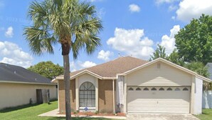 A single-story house with a garage, a palm tree, and a clear blue sky.
