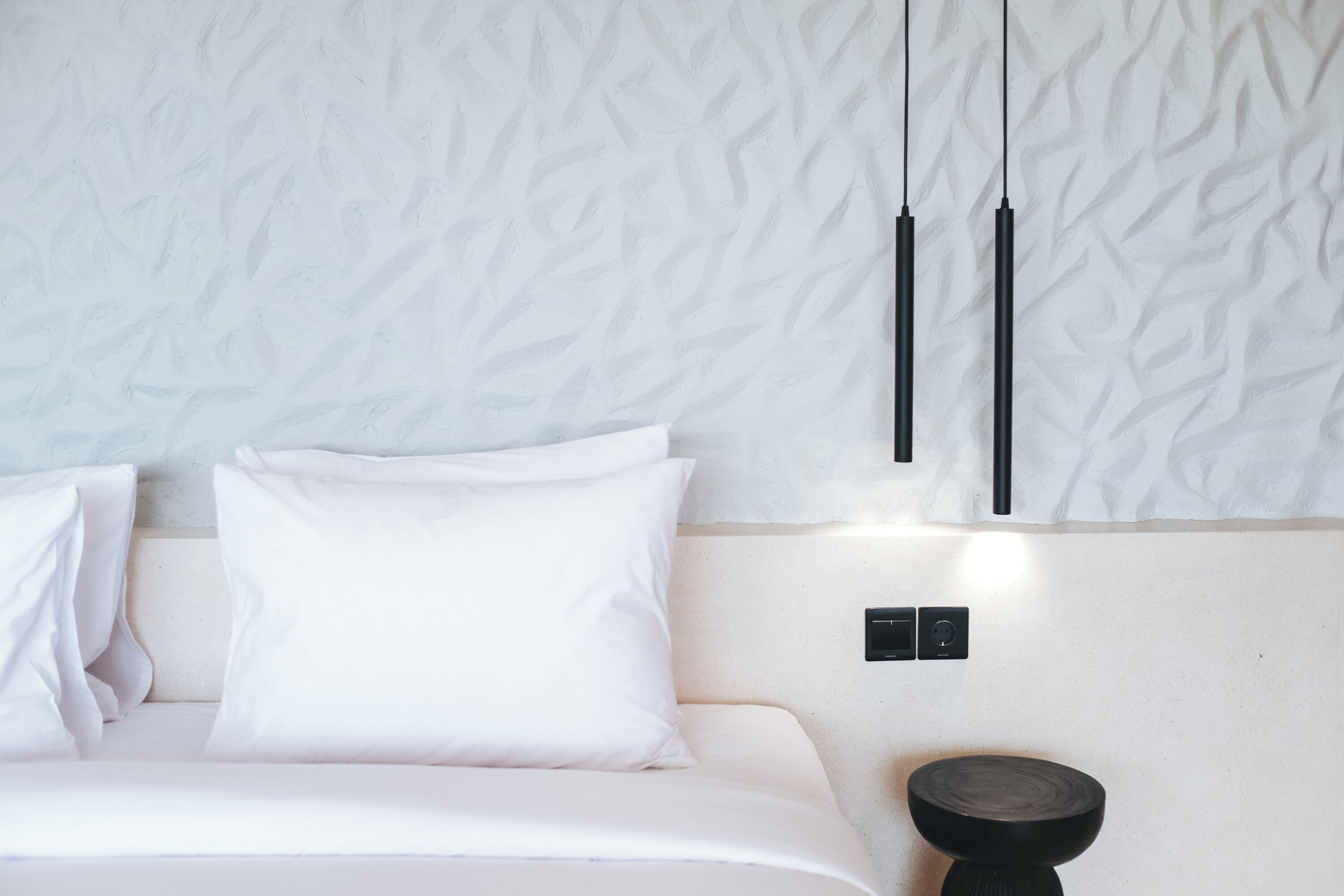 Een moderne slaapkamer met een structuurwand, een bed met witte beddengoed en een minimalistische nachtkastje.