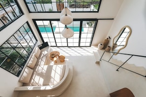 A spacious interior with a curved seating area, a staircase, and large windows overlooking a pool.