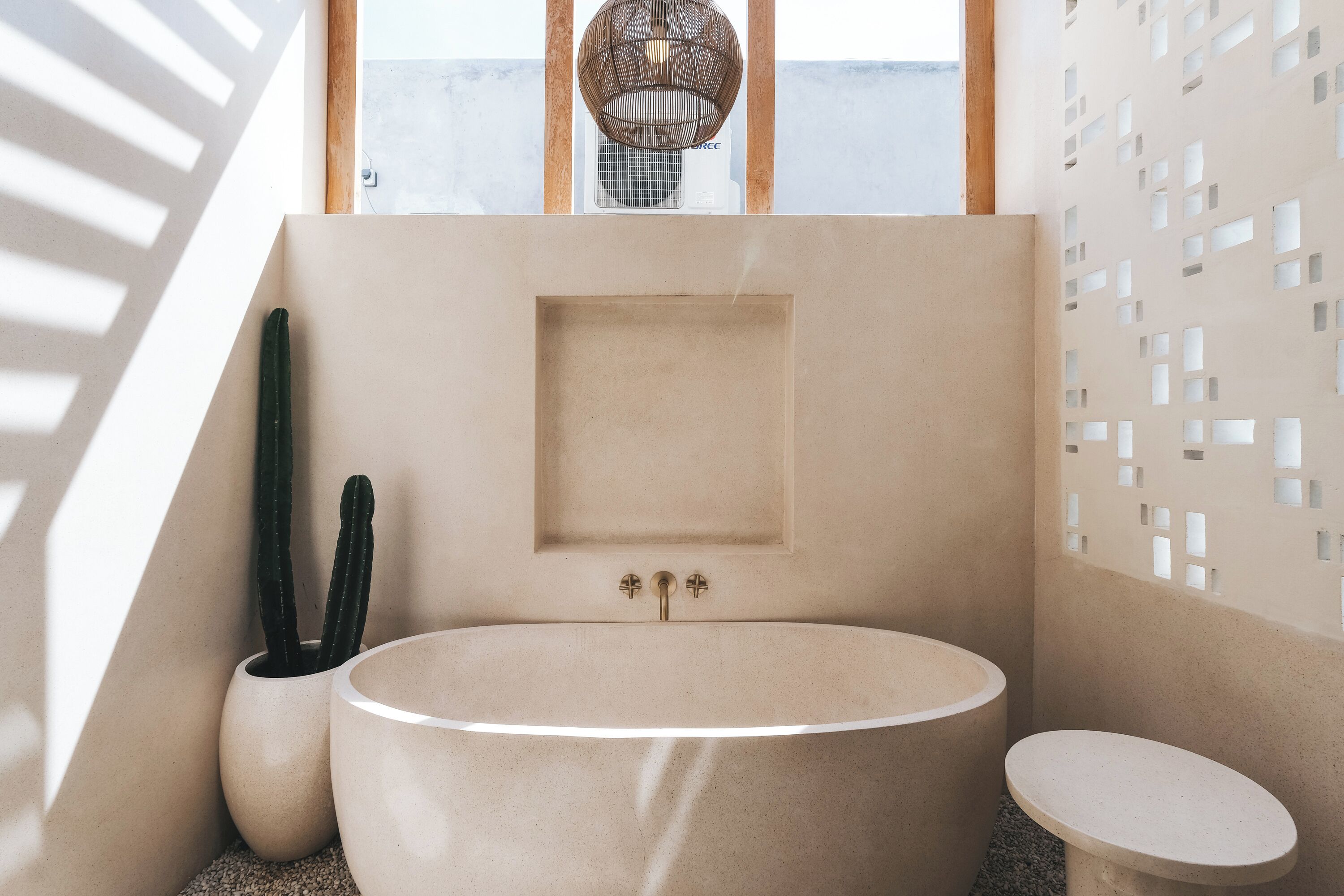 A modern bathroom with a freestanding bathtub, a small sink, and a toilet. There is a cactus in a pot and a decorative light fixture above the bathtub.