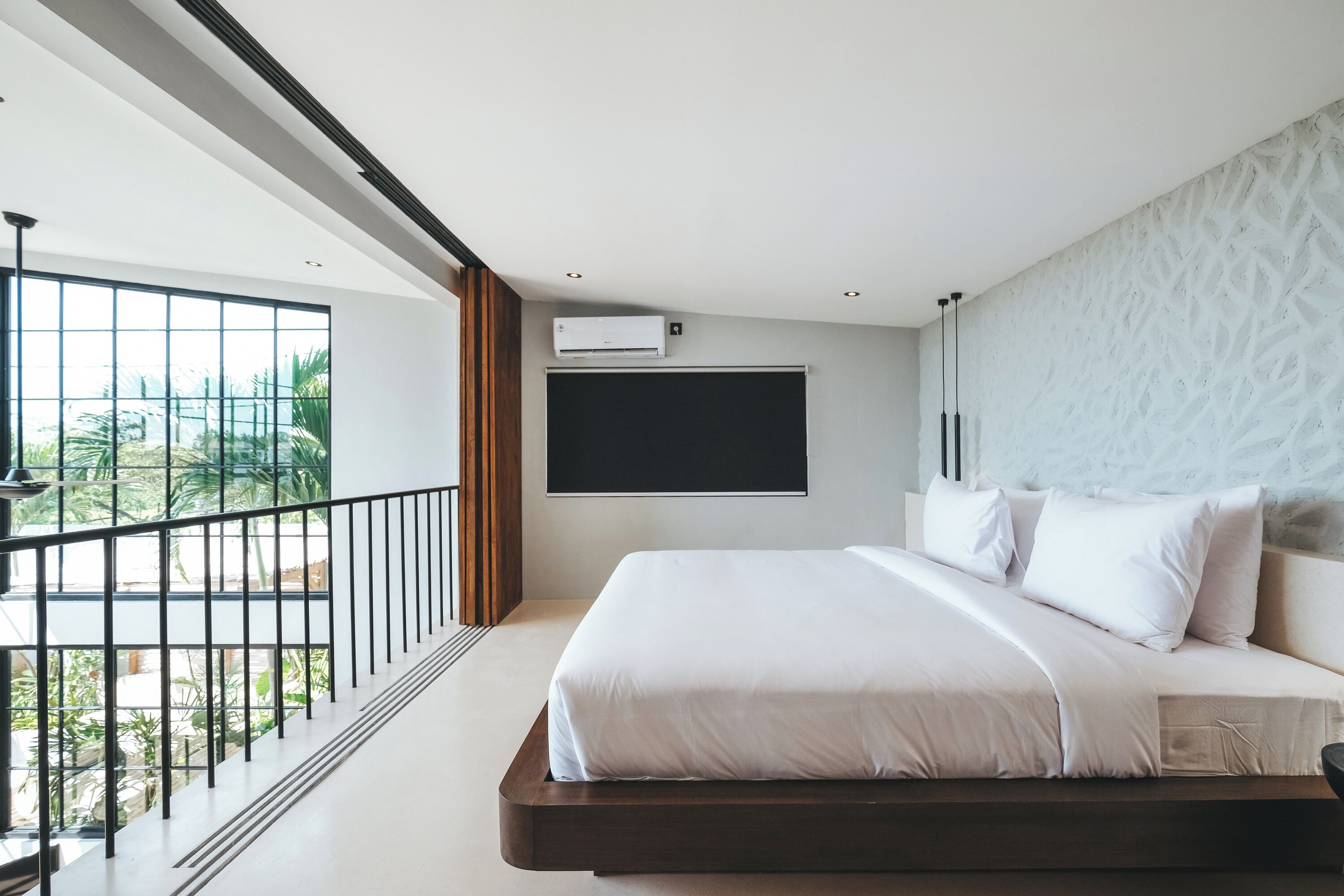 Un dormitorio moderno con una cama grande, un balcón con barandilla y un equipo de aire acondicionado en la pared.