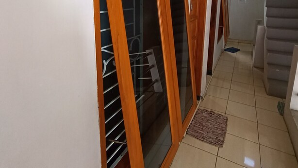 A hallway with a staircase, a wooden door with glass panels, and a tiled floor. - Hotel O Penginapan Hj Lilis Syariah (Sukabumi)