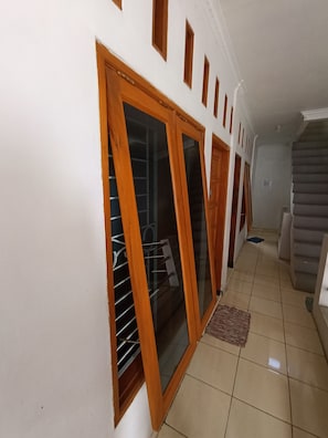 A hallway with a staircase, a wooden door with glass panels, and a tiled floor. - Hotel O Penginapan Hj Lilis Syariah (Sukabumi)
