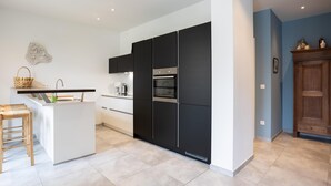Cozinha moderna com ilha central, armários pretos e eletrodomésticos de aço inoxidável.
