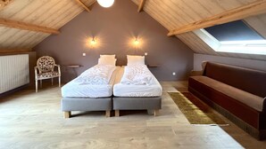 Quarto com teto inclinado, duas camas, uma cadeira, um banco e um claraboia.