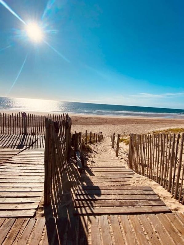 A wooden boardwalk leading to a beach with a clear sky and sun shining.