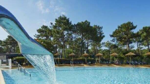 A swimming pool with a water slide, surrounded by trees and umbrellas.
