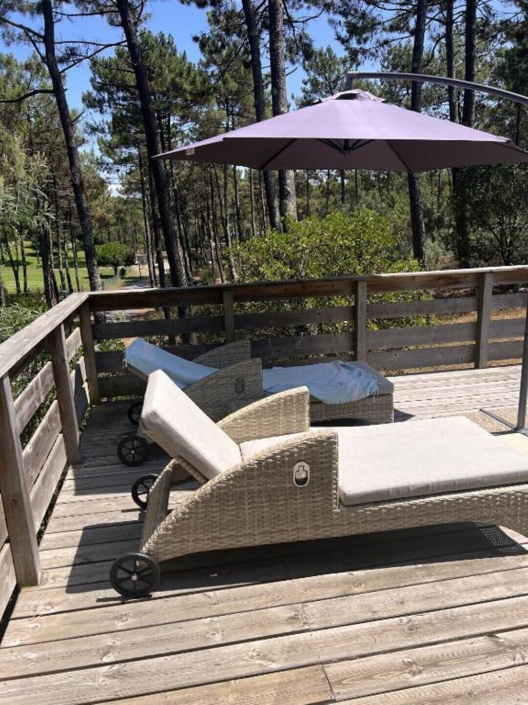 Une terrasse en bois avec des fauteuils de jardin en osier et un parasol violet.