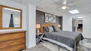 A bedroom with a bed, bedside tables, a dresser, a ceiling fan, and a large mirror. - Eagle's Nest - Upscale Loft,Downtown,Close to GSU! (Statesboro)
