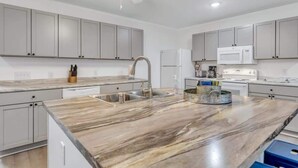 A modern kitchen with grey cabinets, a marble countertop, a built-in sink, and a ceiling fan. - Eagle's Nest - Upscale Loft,Downtown,Close to GSU! (Statesboro)