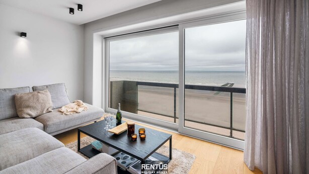 Ein modernes Wohnzimmer mit einer großen Schiebeglasdoor, die auf einen Balkon mit Meerblick führt.