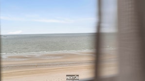 Blick auf einen Strand durch ein Fenster mit dem RENTUS Urlaubswohnungen Logo.