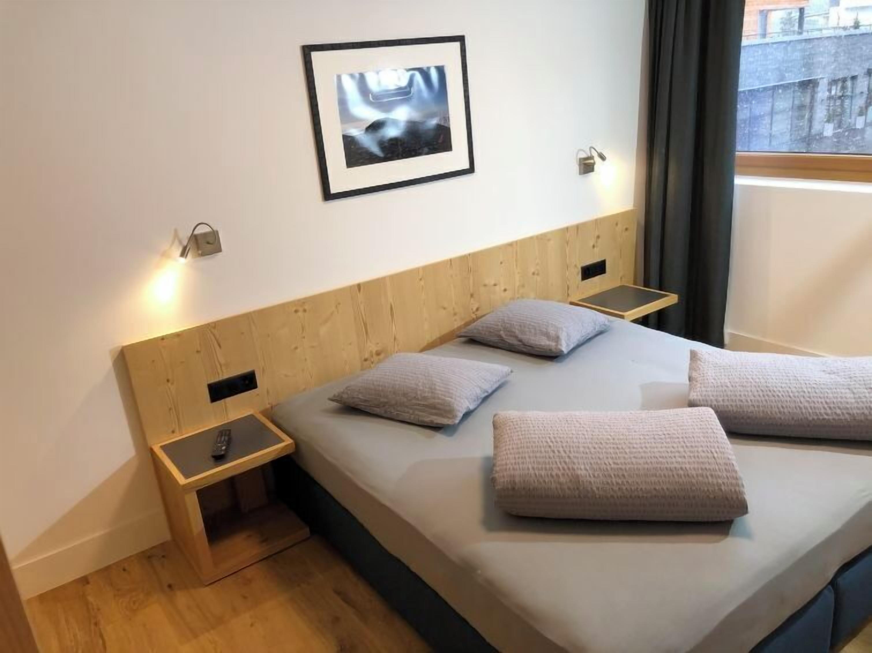 Ein modernes Schlafzimmer mit einem Holzkopfteil, einem Bett mit zwei Kissen, einem Nachttisch und einem gerahmten Bild an der Wand.