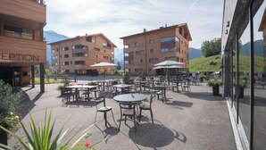 A hotel courtyard with outdoor seating, multiple buildings, and a mountainous backdrop. - Catrina 3-Zimmer Premium Apartment by Interhome (Disentis)
