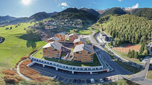 A modern building with a central courtyard, surrounded by parking and roads, set in a mountainous area with greenery and distant hills. - Catrina 3-Zimmer Premium Apartment by Interhome (Disentis)