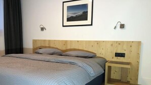 A bedroom with a wooden headboard, a bed with grey bedding, a nightstand with a lamp, and a framed picture on the wall. - Catrina 3-Zimmer Premium Apartment by Interhome (Disentis)