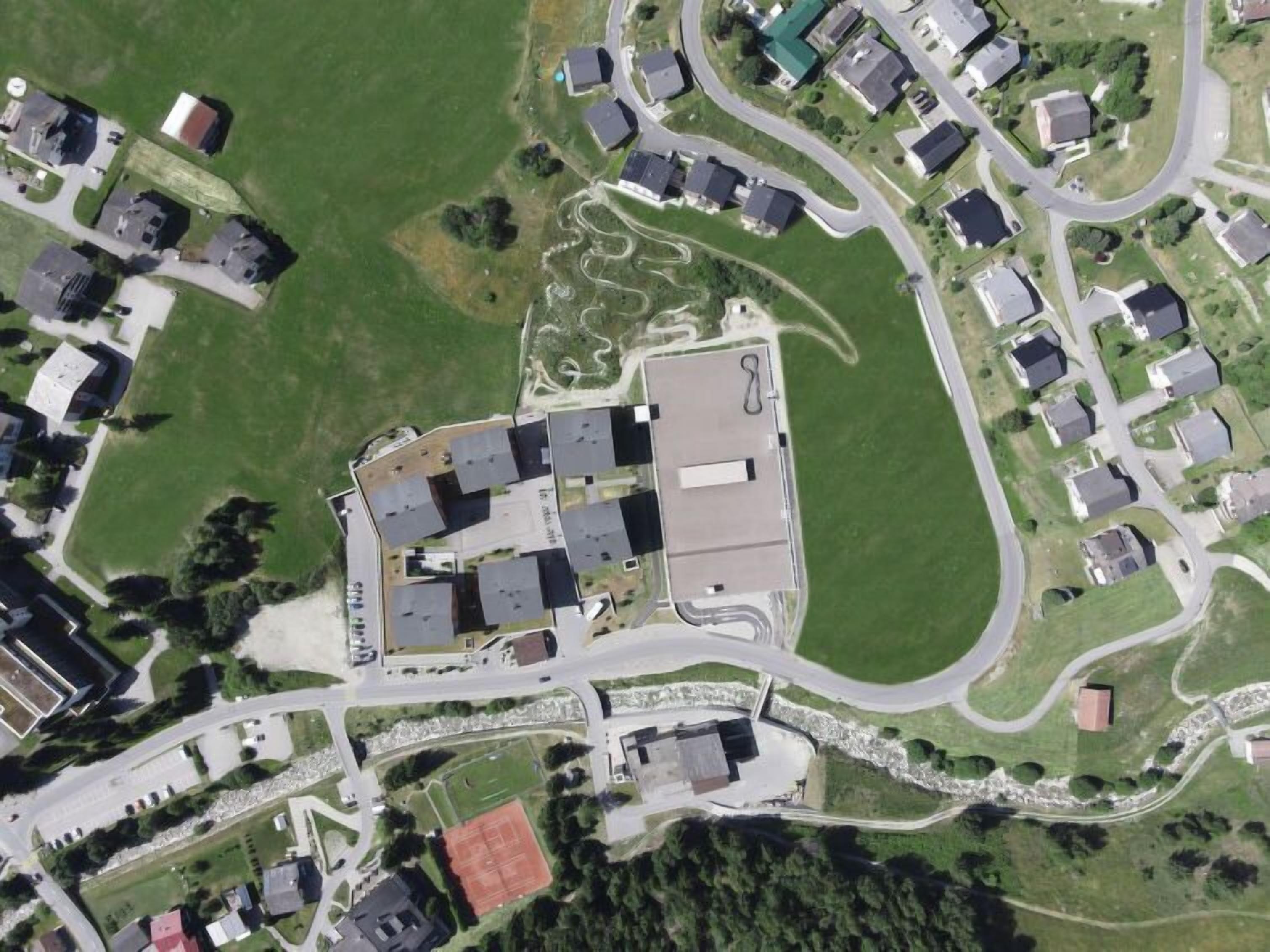 An aerial view of a residential area with houses, roads, and a large building with a parking lot.