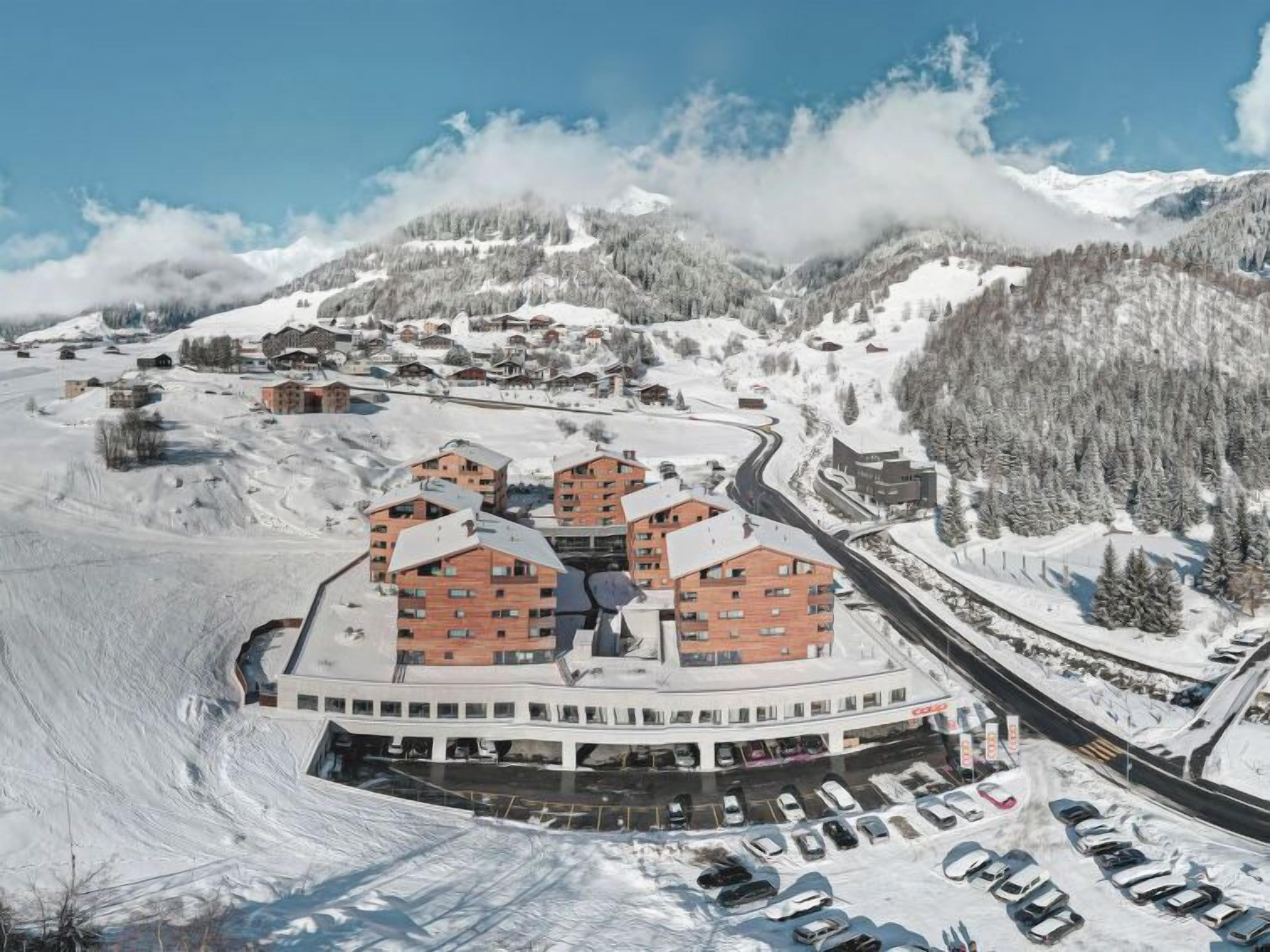 Een skigebied bedekt met sneeuw, met meerdere gebouwen, waaronder een centraal hotel en een parkeerplaats.