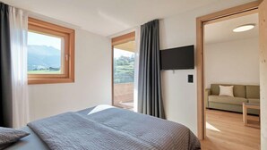 A bedroom with a bed, a TV mounted on the wall, and a view of the outdoors through a window.