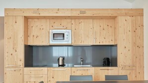 A compact kitchen with wooden cabinets, a microwave, a kettle, and a coffee maker. There is a dining table with chairs.
