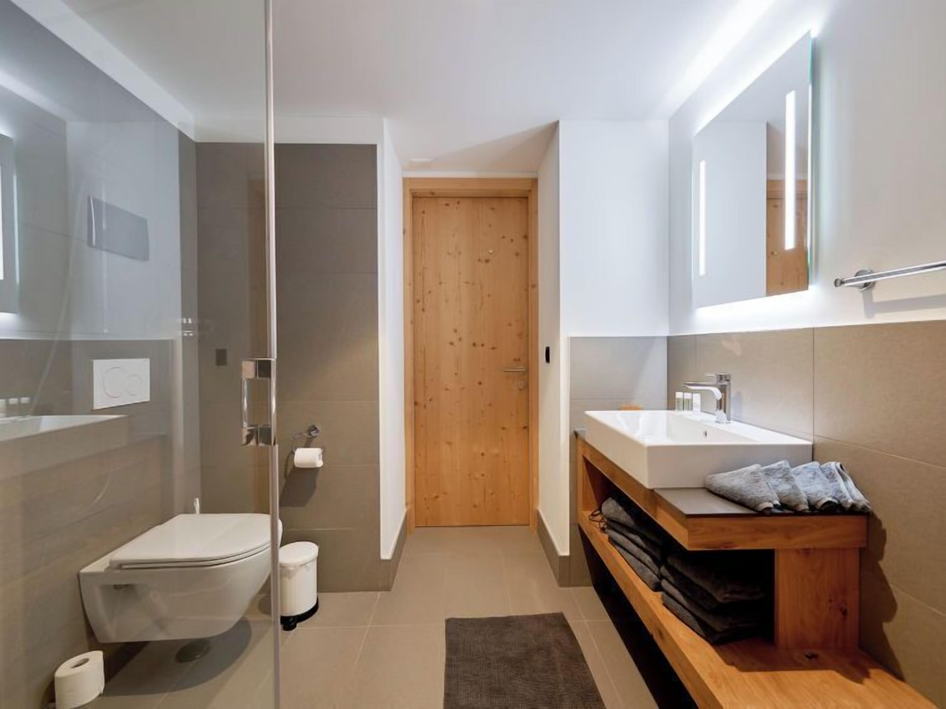Ein modernes Badezimmer mit einer Duschkabine aus Glas, einer Holztür, einer weißen Toilette und einem Holzwaschtisch mit Handtuchhalter.