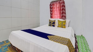 A neatly made bed with a white and blue bedspread, two patterned pillows, and a red curtain. - Hotel O Guest House Pak Darso (Kalijambe)