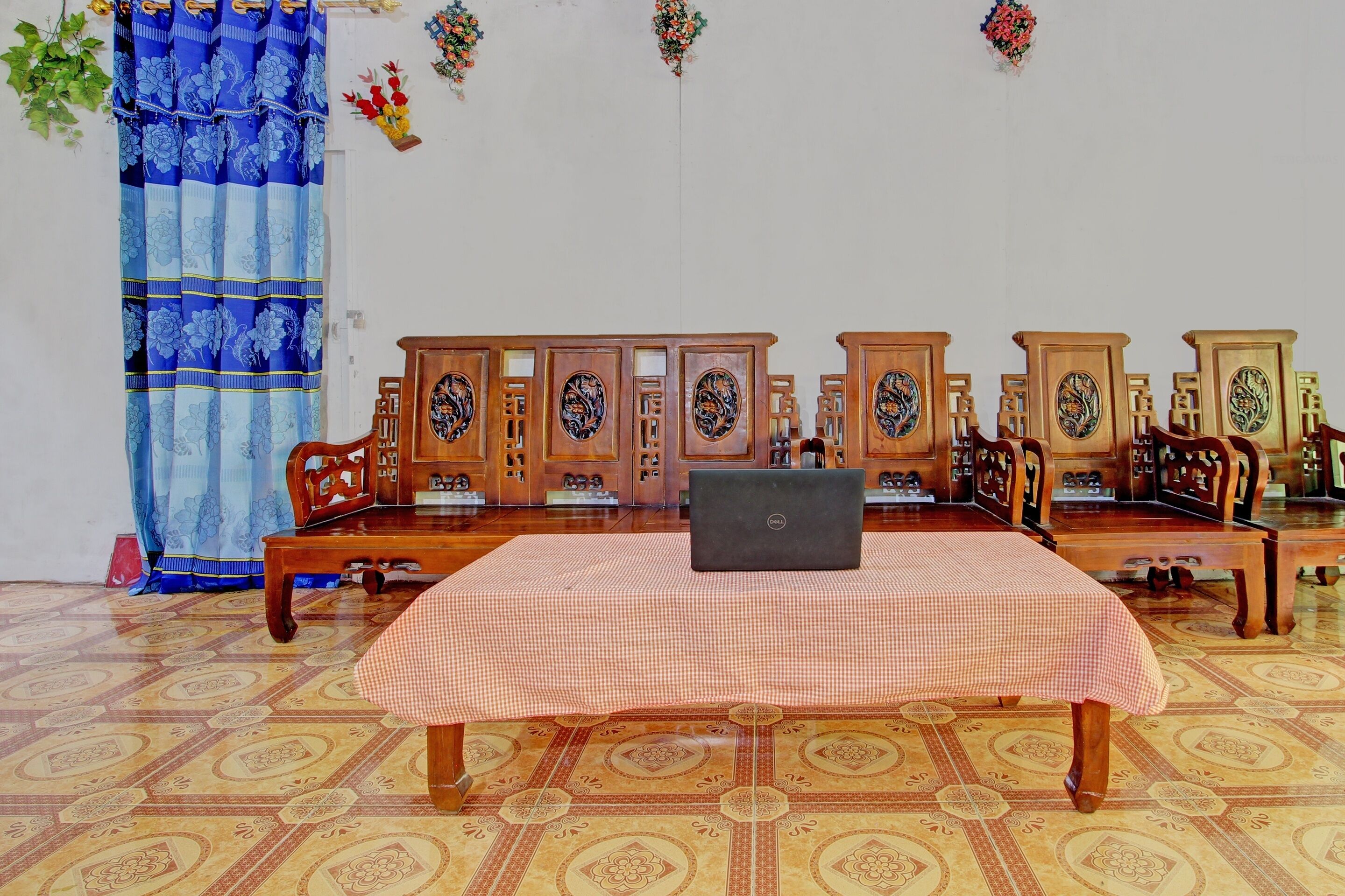 A room with a checkered table, a laptop, traditional wooden furniture, and patterned flooring.