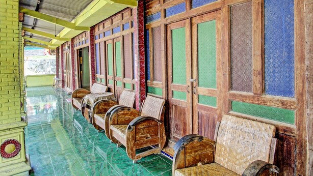 A row of wooden benches with woven seats and backs, arranged along a corridor with a tiled floor and wooden doors with glass panels. - Hotel O Guest House Pak Darso (Kalijambe)