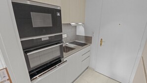 Een kleine keuken met een inbouwoven, een spoelbak en witte kastjes.