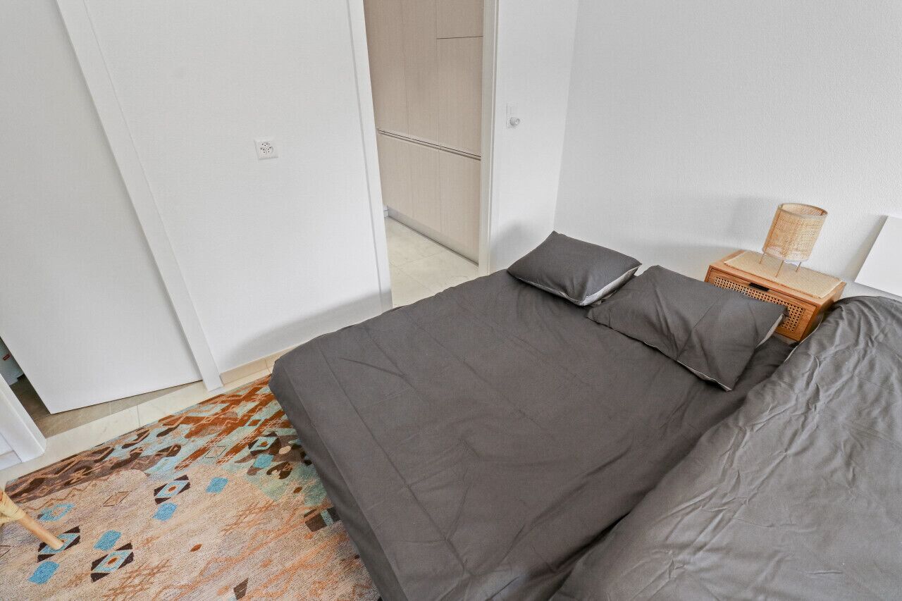 Een slaapkamer met een bed, kussens, een nachtkastje met een lamp en een kamerbreed tapijt.