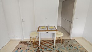 Een kleine kamer met een witte deur, een witte tafel met twee stoelen en een kamerkleed met een patroon.