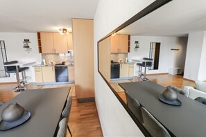 Una cocina moderna con armarios de madera, un comedor con mesa y sillas, y un espejo que refleja el ambiente.