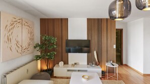A modern living room with a flat-screen TV, a white sofa, a small coffee table, and a potted plant. - Logement chaleureux au coeur de la station (Crans-Montana)