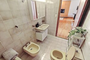 Een kleine badkamer met een toilet, wastafel, spiegel en een bidet.