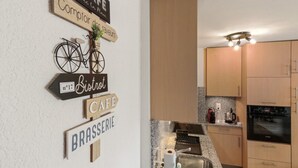 A kitchen with wooden cabinets, a built-in oven, and a countertop with a coffee maker and other appliances. - Logement chaleureux au coeur de la station (Crans-Montana)