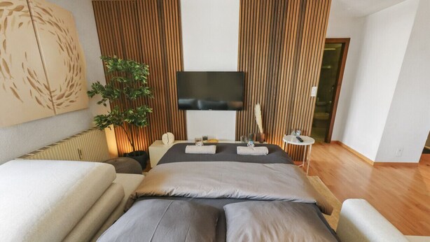 A modern bedroom with a large bed, a flat-screen TV, and a wooden panel wall. - Logement chaleureux au coeur de la station (Crans-Montana)