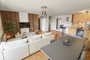 Una sala de estar moderna con un sofá grande, una mesa de comedor y una cocina con armarios de madera y horno empotrado.