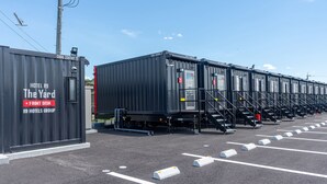 A row of black modular hotel units with a sign indicating "Hotel R9 The Yard" and "Front Desk" pointing to the left. - HOTEL R9 The Yard Tomioka (Tomioka)