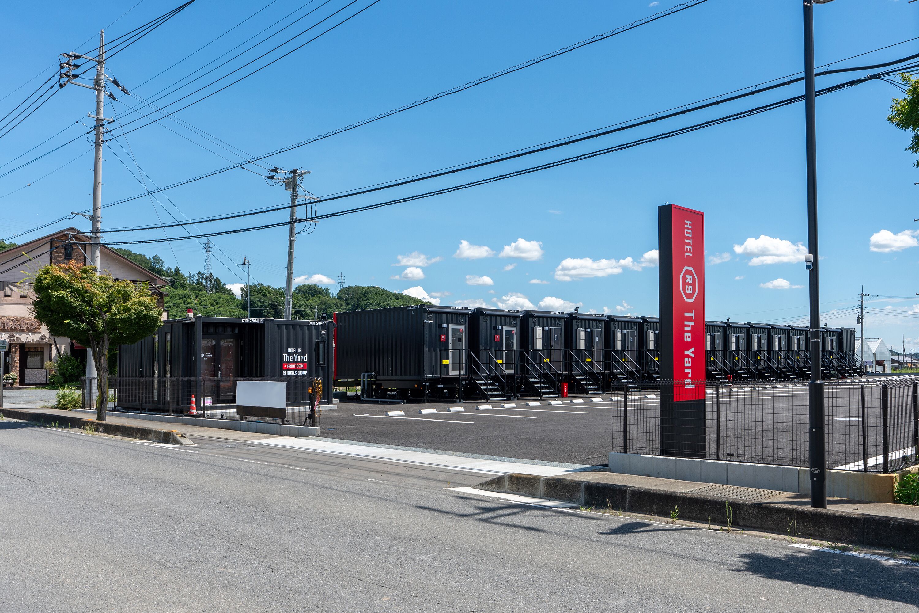 A hotel with a red sign, a parking lot, and a train station in the background.